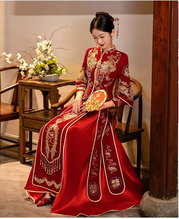 Woman in aRed Qun Kwa – Traditional Chinese Wedding gown sitting in a room with wooden furniture and flowers.