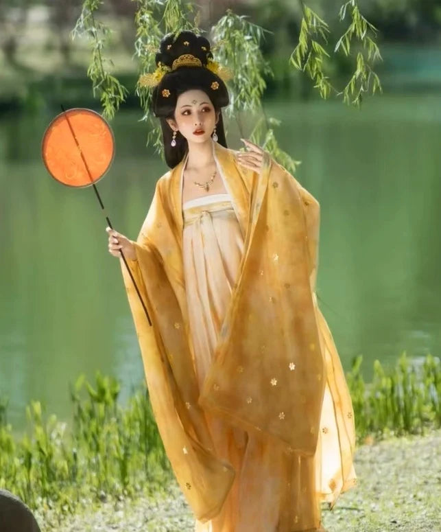 Woman in traditional yellow Golden Traditional Chinese Tang Dynasty Hanfu Dress Set  garment holding a fan by a body of water