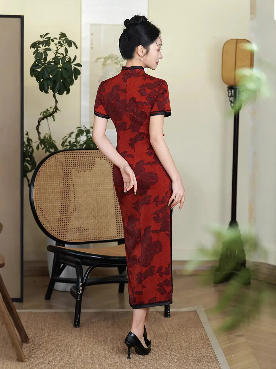 Woman wearing a Deep Red Floral Qipao Cheongsam Dress with Black Trim  in an indoor setting with plants and furniture.