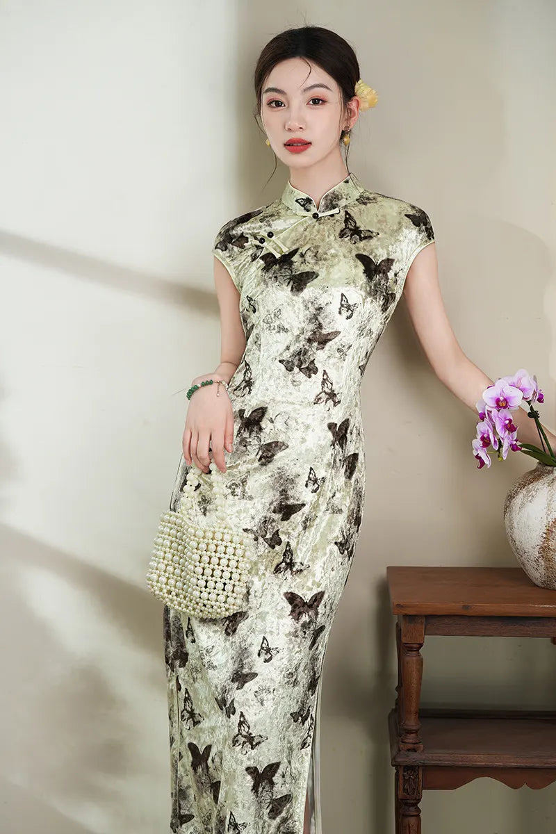 Woman in an Elegant Velvet  chinese cheongsam Dress with Butterfly Print  holding a flower, standing next to a wooden table with a vase.