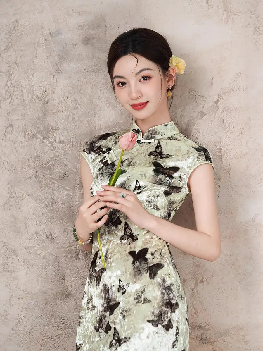 Woman in a Elegant Velvet cheongsam Dress with Butterfly Print  holding a flower against a textured wall.