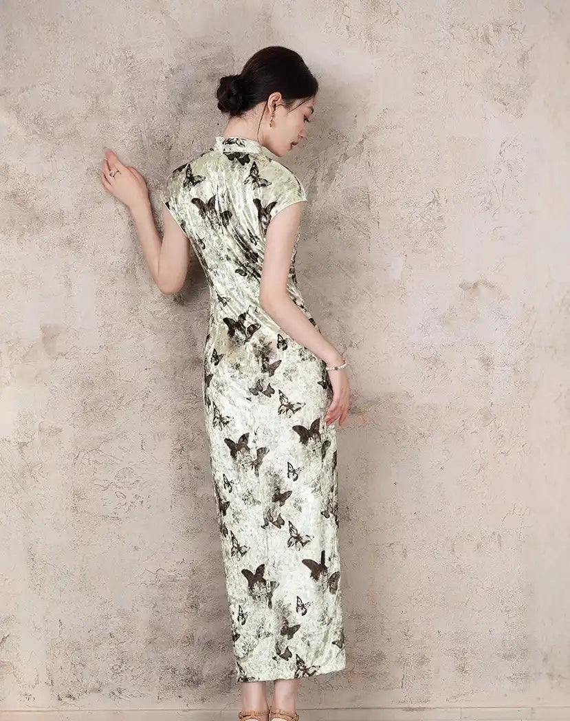 Woman wearing a Elegant Velvet Qipao gown with Butterfly Print against a textured wall