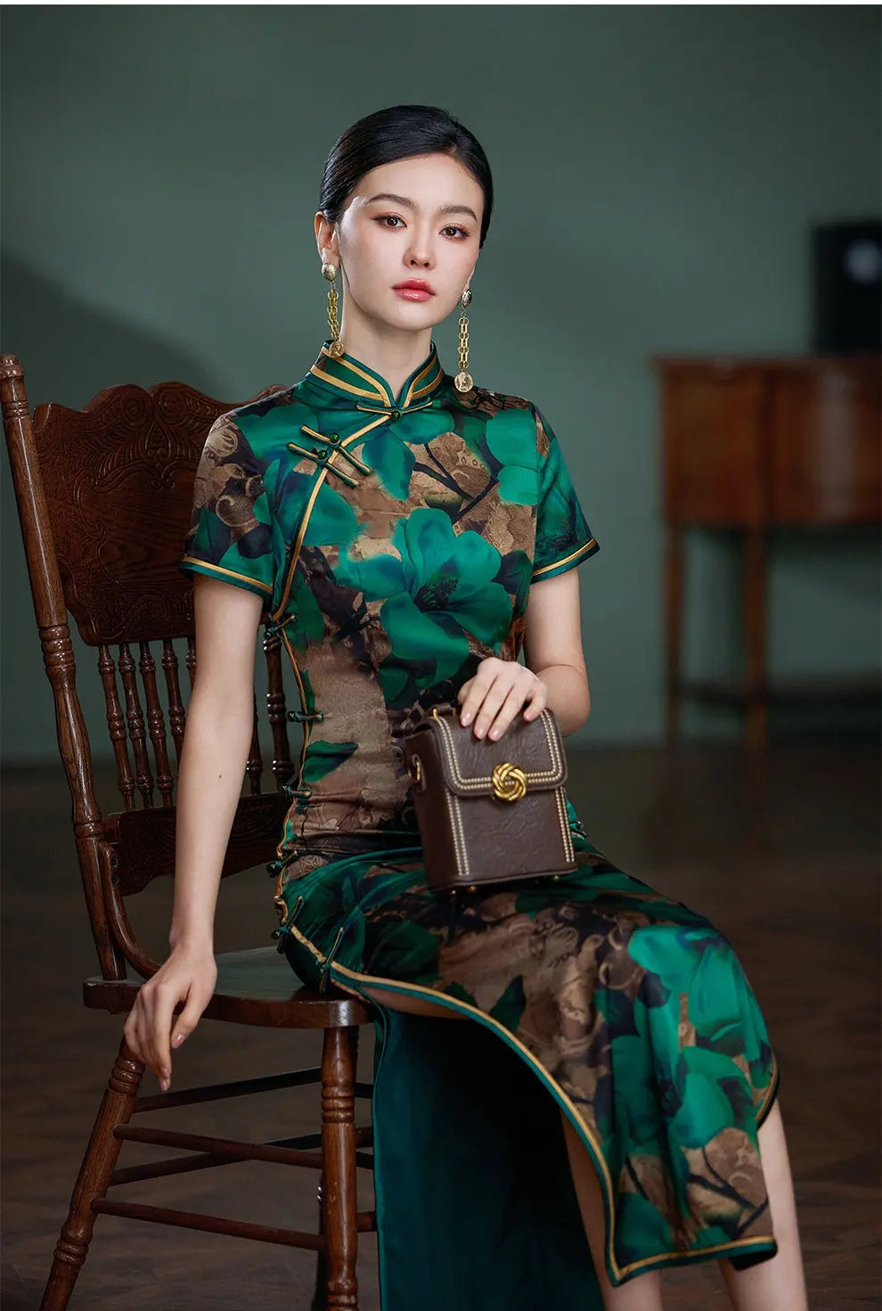 Woman in a Emerald Green Floral Silk Chinese Qipao Cheongsam Dress sitting on a wooden chair.