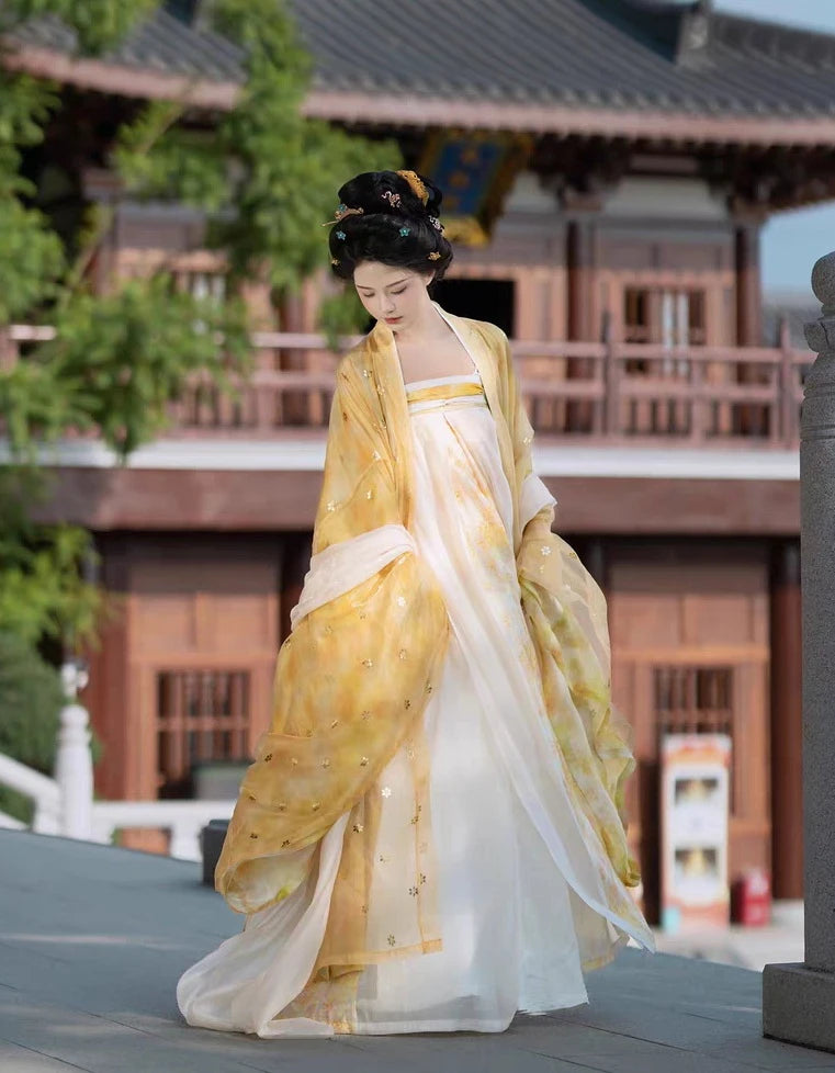 Woman in traditional yellow and Golden Traditional Chinese Tang Dynasty Hanfu Dress Set  standing in front of a wooden building.