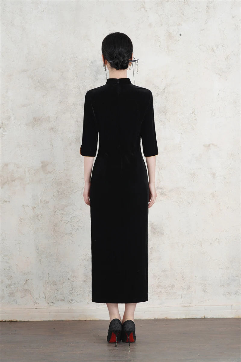 Person wearing a Long Sleeves Black Velvet Qipao Dress with Gold Accents standing against a light gray wall.