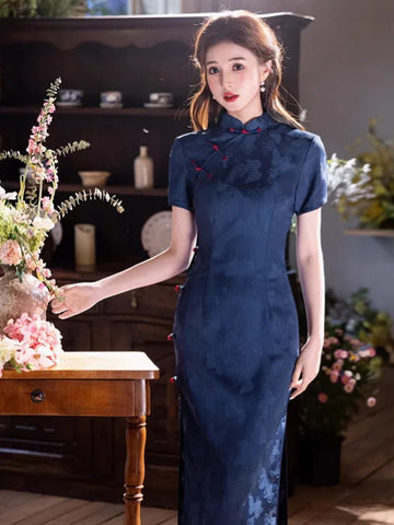 Woman in a Navy Blue Jacquard Butterfly Cheongsam – Mid-Length Modern Qipao standing in a room with flowers and furniture.