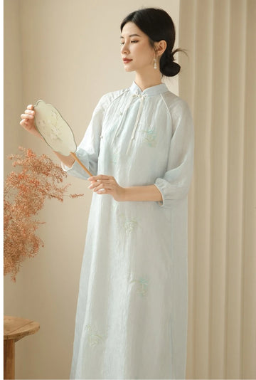 A Chinese Woman in aZen-Inspired Light Blue Loose Cheongsam Qipao Dressholding a dried flower arrangement against a beige background
