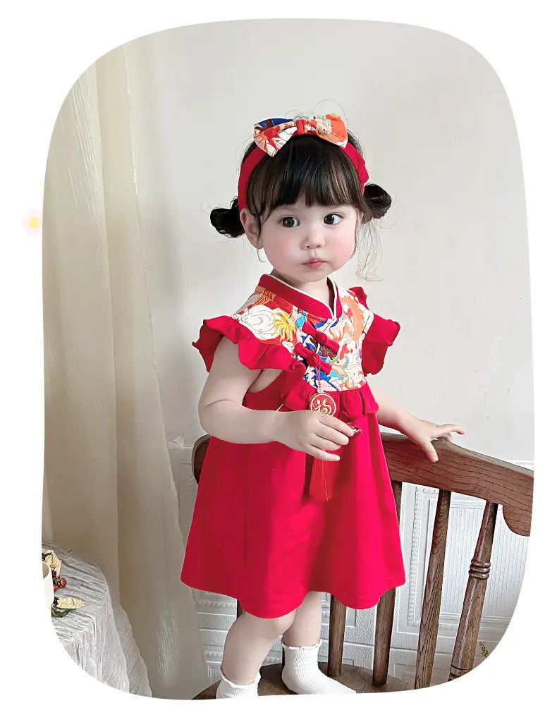 Child wearing a red dress with a colorful top, sitting on a chair.