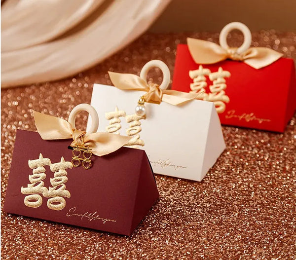 Three Luxury Gold Foil Double Happiness Favor Boxes for Chinese Wedding  with gold ribbons and Chinese characters on a glittery surface.