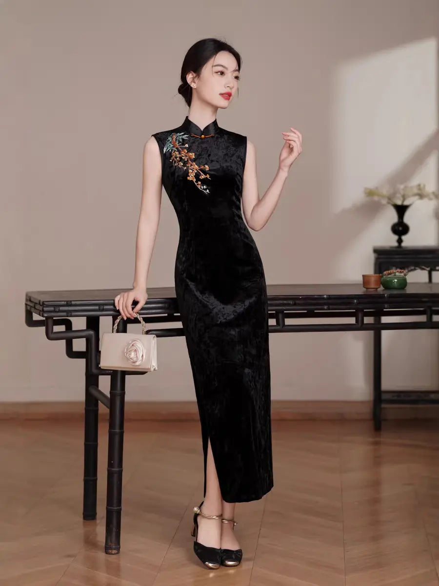 Woman in aBlack Modern Velvet Sleeveless Embroidered Qipao  dress with floral embroidery standing in a room with wooden floor and table.
