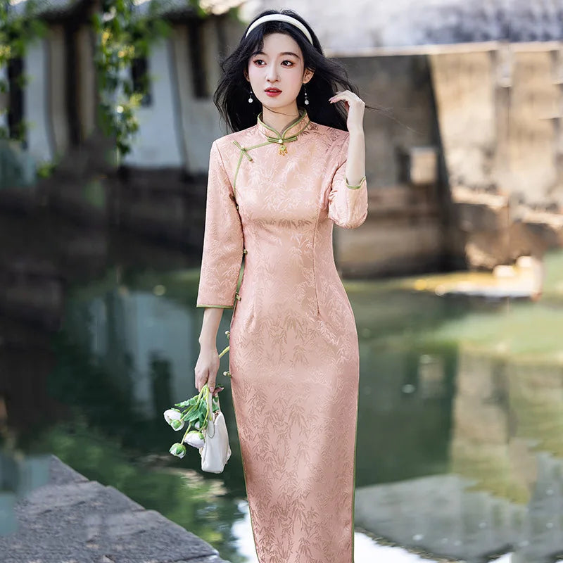 Woman in a  traditional Blush Pink Long Sleeves Qipao Cheongsam Dress with Bamboo Pattern  standing by a body of water with greenery.