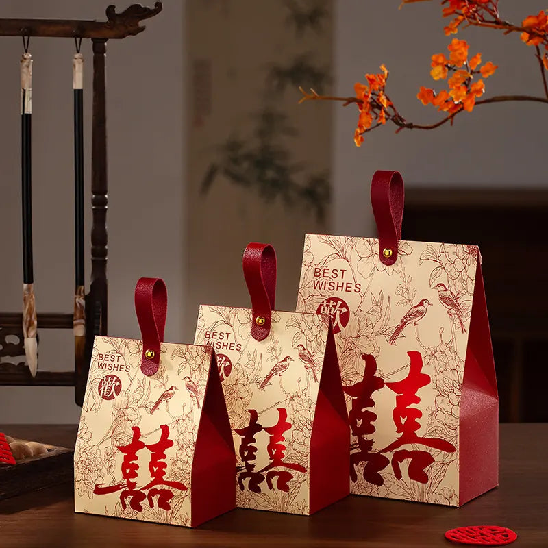 Three  Double Happiness Chinese Wedding Favor Box  with red handles on a wooden surface, featuring Chinese characters and traditional designs.