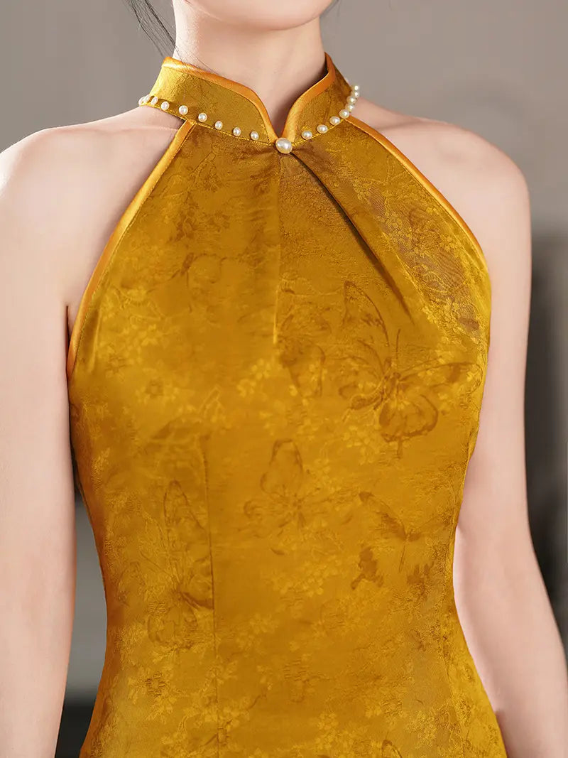 A close-up of a woman wearing a sleeveless Pearl-Trimmed Sleeveless Halter Jacquard Satin Qipao  cheongsam-style top in rich golden yellow fabric with a subtle tonal floral and butterfly pattern, featuring a pearl-trimmed collar and a single front button.