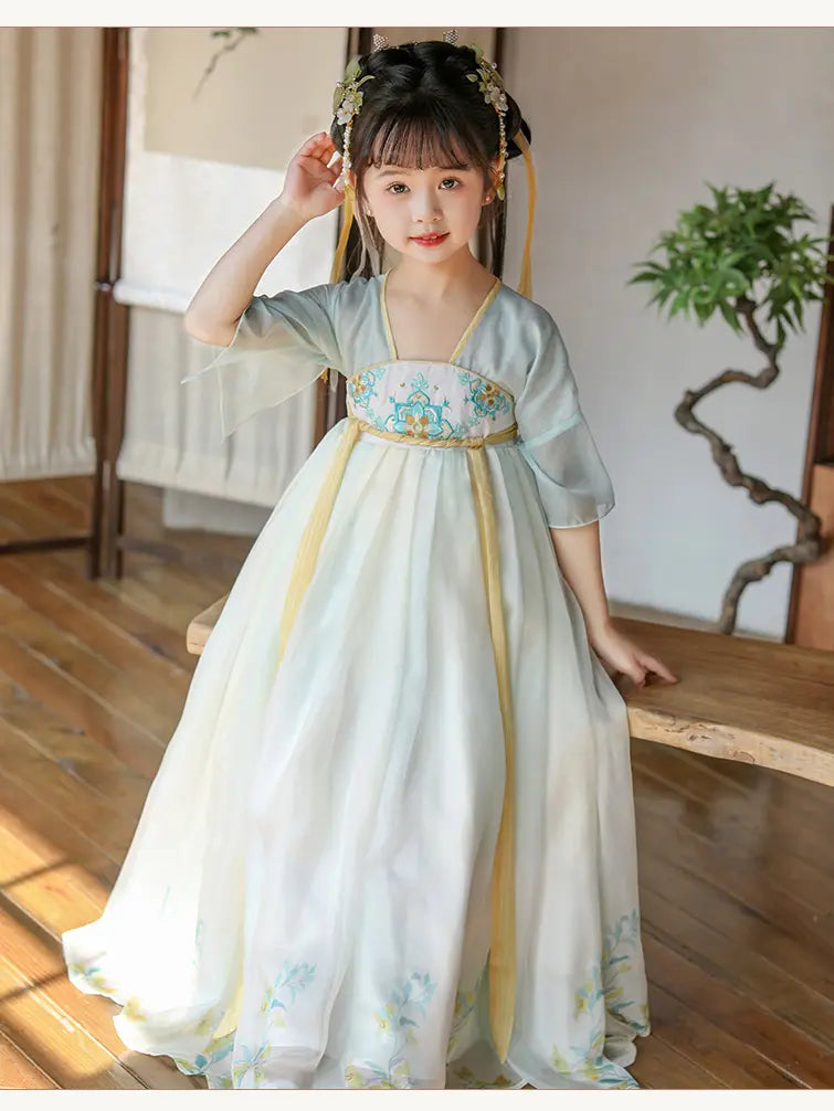 Young girl in a traditional Light Blue Girls Chinese Tang Dynasty Style Fairytale Hanfu Dress  with floral patterns in a room with wooden floor and white wall.