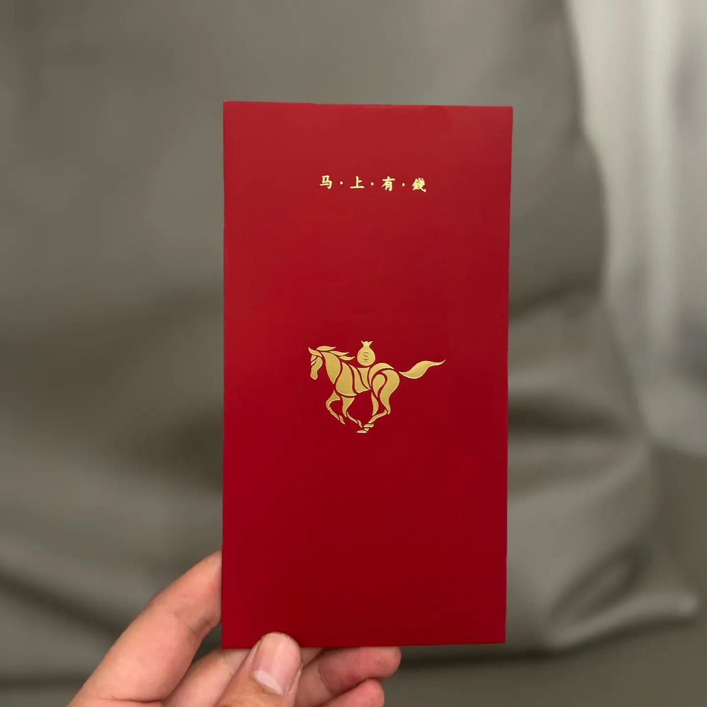 Minimalist 2026 Year of the Horse Red Envelopes - Lucky Money Packets  with gold horse design and text held by a hand against a gray background