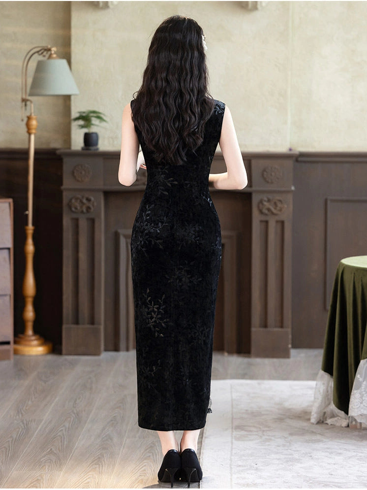 A woman stands with her back to the camera wearing a sleeveless black long dress with a textured floral pattern, set in an indoor room with a fireplace and wooden paneling.