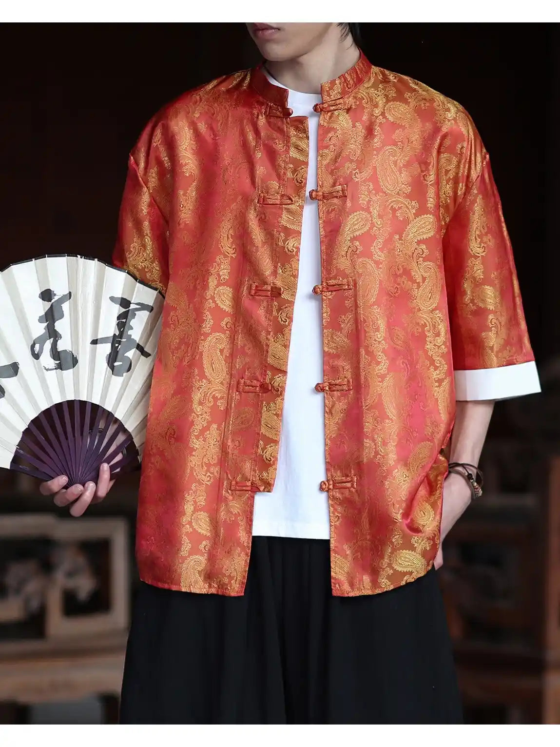 Person wearing a traditional red and gold patterned Modern New Chinese Style Men's Half Sleeve Jacquard Tang Shirt  jacket holding a fan with Chinese characters.