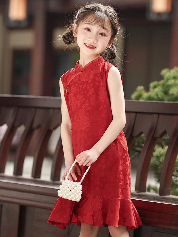 A young girl with braided hair stands outdoors wearing a Red Floral Summer Sleeveless Qipao Dress for Girls dress with a subtle tonal floral pattern. She is holding a small white beaded handbag and posing in front of a dark wooden railing.