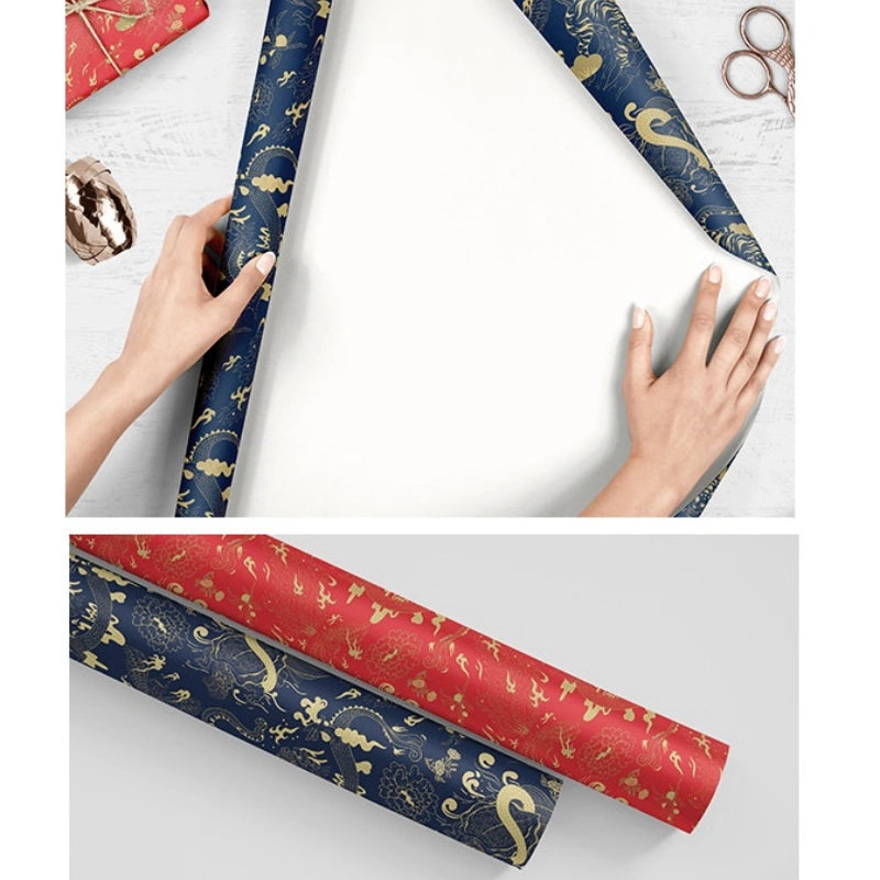 Two rolls of decorative wrapping paper shown on a light surface, with hands holding one roll and a wrapped gift box nearby. The top panel shows navy blue paper with gold floral motifs, and the bottom panel shows a second roll in red with matching gold floral motifs.