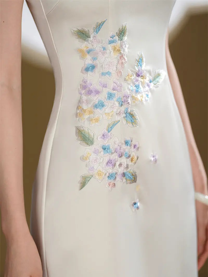 Close-up of a white sleeveless dress with a vertical floral embroidered pattern in pastel blue, purple, yellow, and green on the torso.