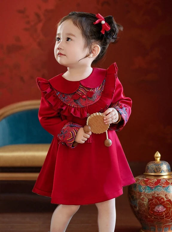 Young girl in a redModern Chinese Baby Qipao Cheongsam Dress with Tassel  holding a toy, standing against a decorative background.