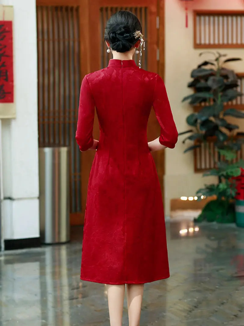 A woman viewed from behind wearing a long-sleeved red cheongsam-style dress in an indoor setting with wooden doors and plants in the background.