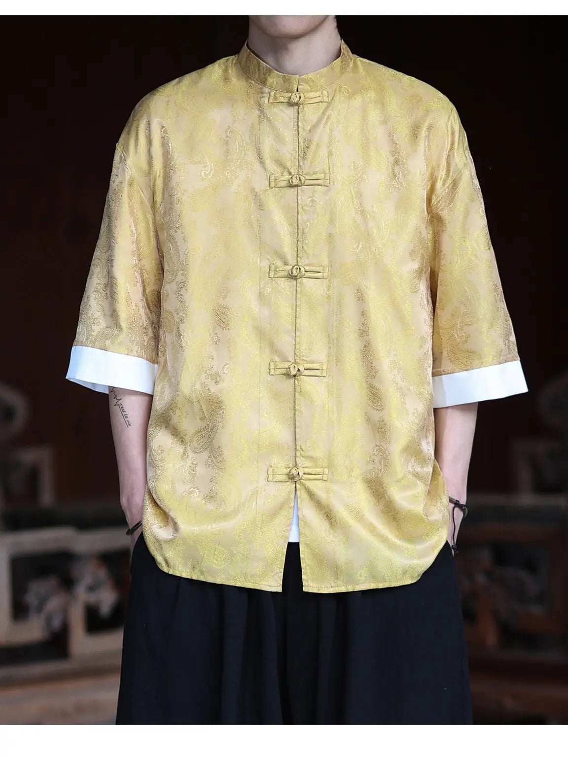 Person wearing a yellow patterned Modern New Chinese Style Men's Half Sleeve Jacquard Tang Shirt with white cuffs and black pants against a dark background