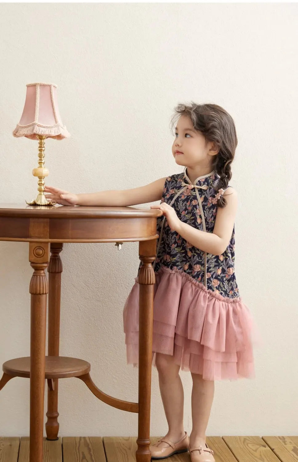 Young girl in a Modern Pink Floral Tulle Qipao cheongsam  Dress standing next to a wooden table with a lamp