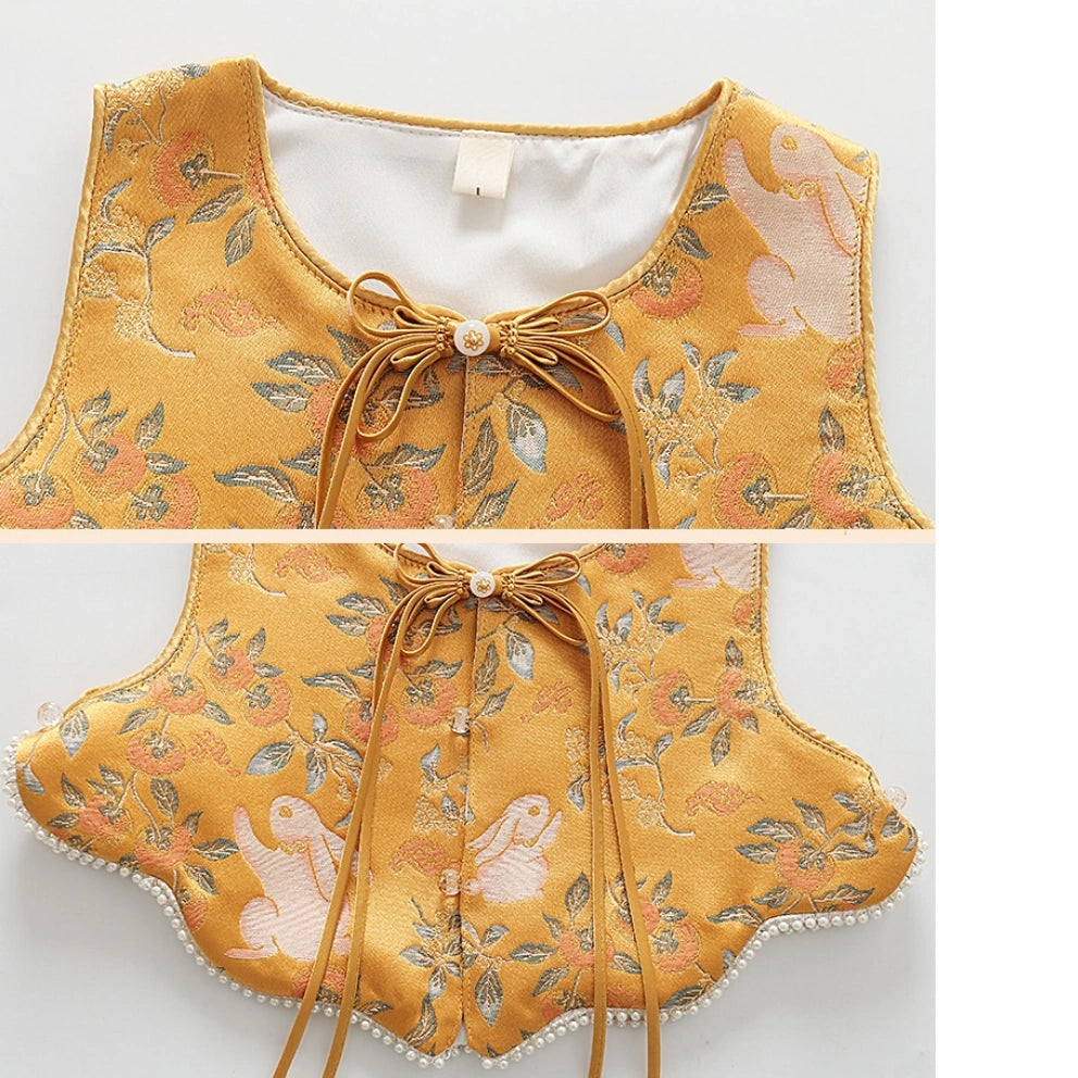 A split-view product shot of a yellow embroidered vest or top with a bow at the neckline, shown against a plain light background. The fabric has floral and bird motifs in muted green, peach, and white, with a scalloped edge and pearl-like trim.