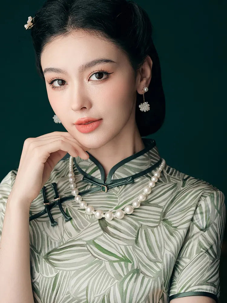 Woman wearing a traditional chinese green qipao cheongsam  dress with leaf patterns and pearl necklace against a dark background