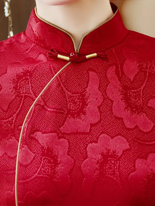 Close-up of a red embroidered traditional Chinese cheongsam jacket with gold trim and a cordong closure, shown on a mannequin torso.