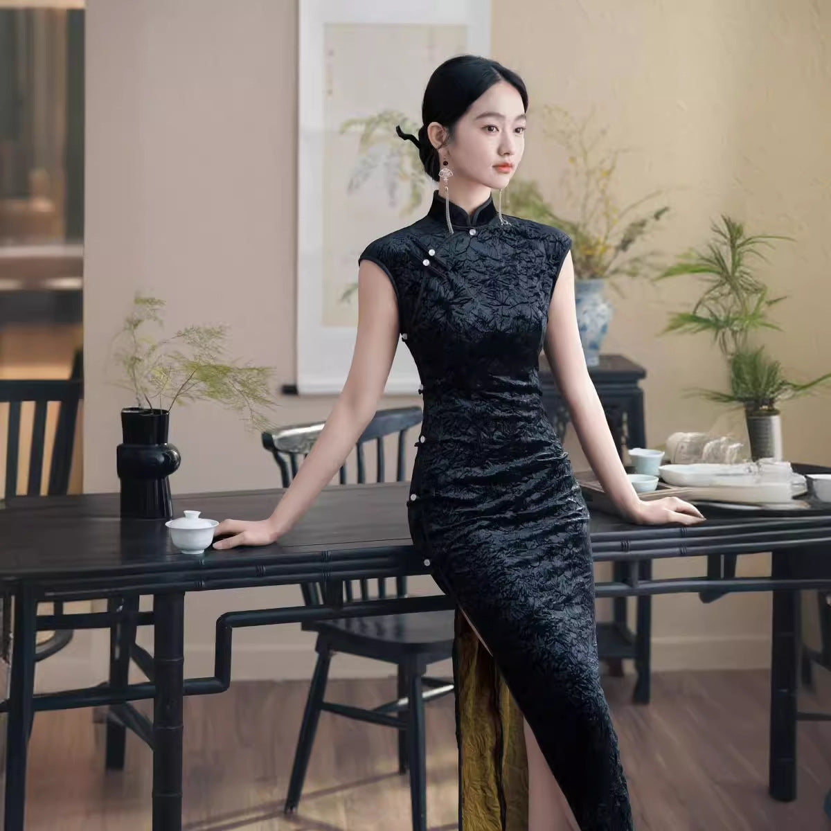 Model in black velvet sleeveless qipao cheong dress next to a table 