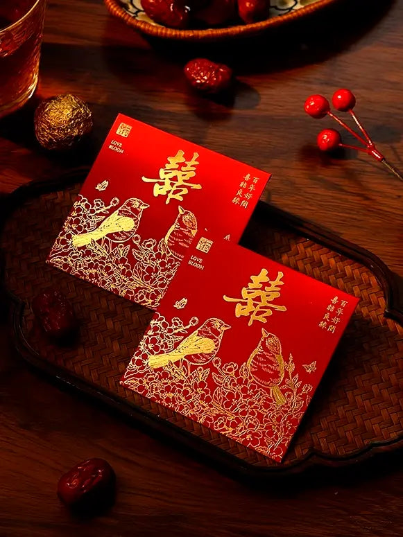 Two double happiness wedding red envelopes with gold designs on a wooden surface with red berries.