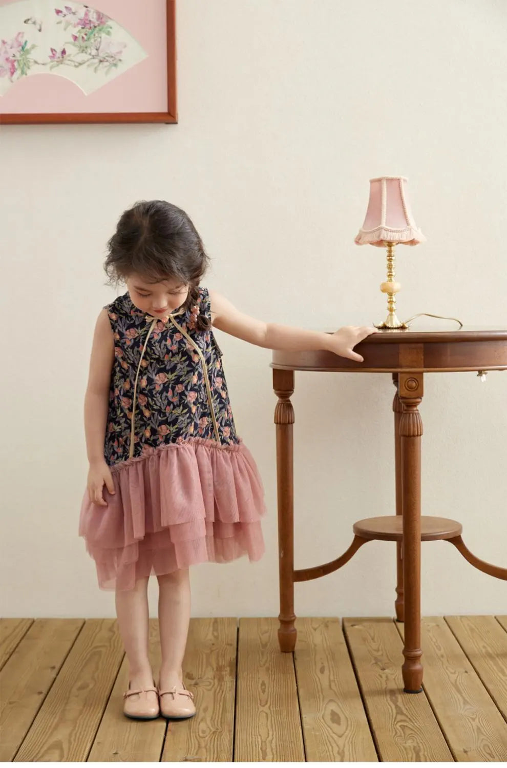 Young girl in a Modern Pink Floral Tulle Qipao cheongsam Dress standing next to a small wooden table with a lamp.