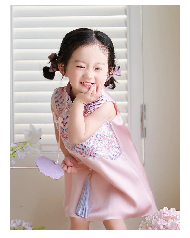 Young girl in a pink Girls' "Good Fortune" Traditional Sleeveless A-Line Jacquard Qipao dress standing in front of white blinds