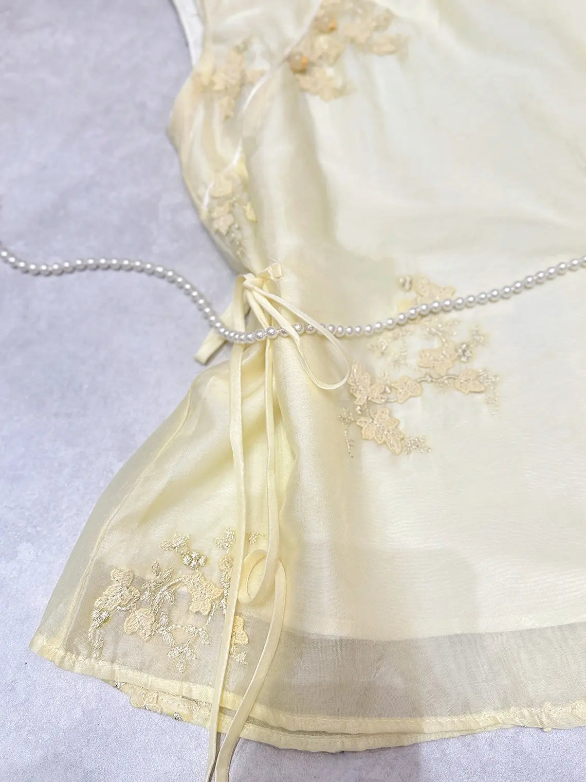 yellow New Chinese Style - Sleeveless Asymmetric Top & Maxi Skirt Set  dress with floral embroidery and a pearl belt on a light gray background