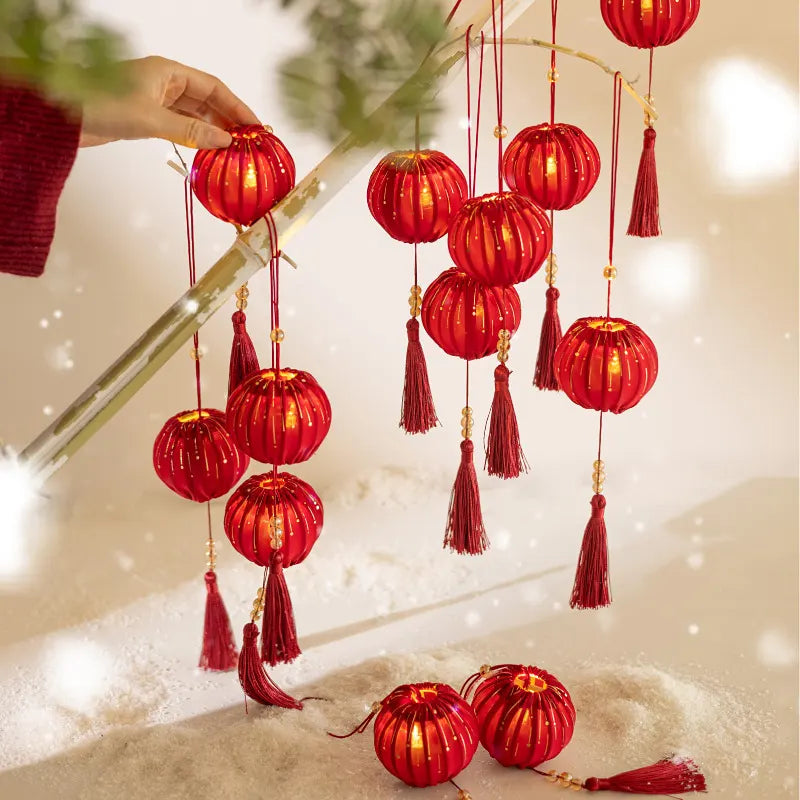 Red lanterns with tassels hanging from a branch in a snowy setting