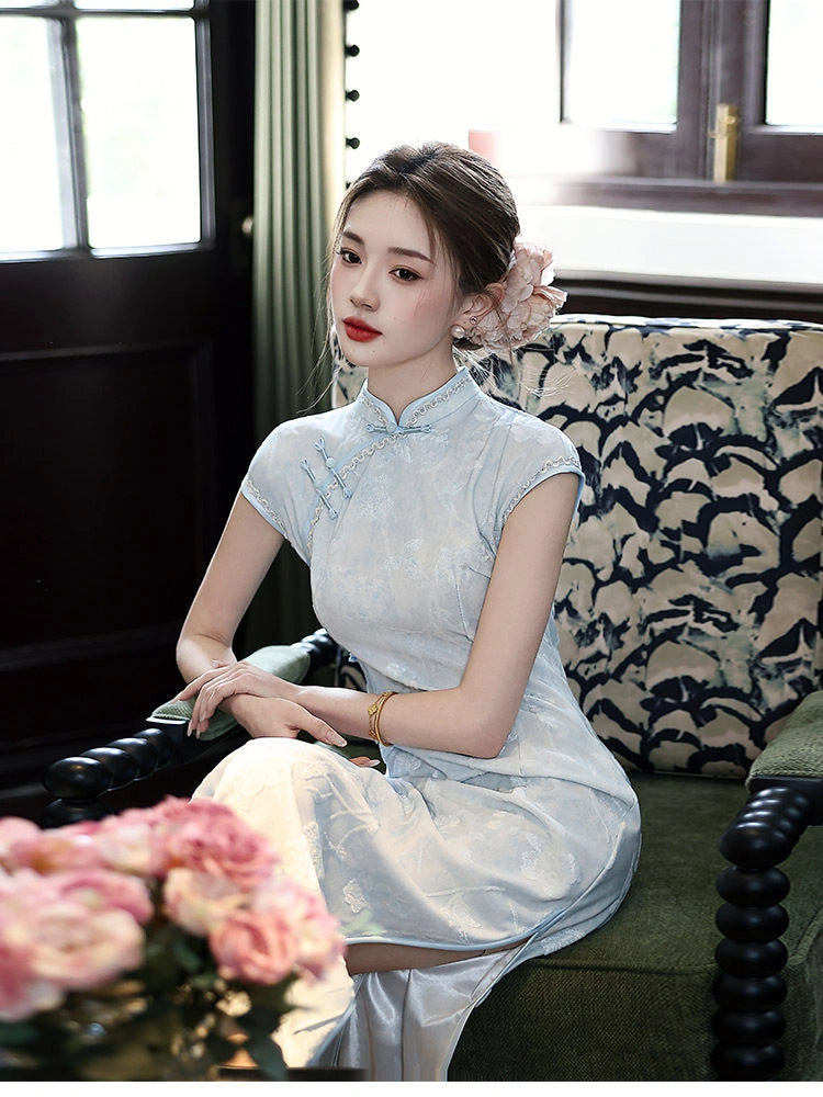 Woman in a light blue Vintage Floral Burnout Velvet Jacquard Qipao dress sitting on a couch with flowers in the foreground