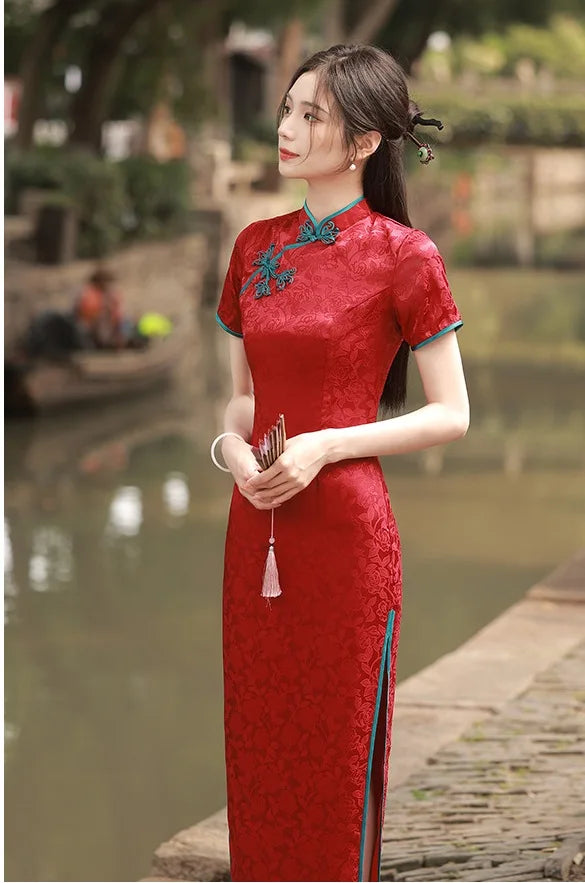 Woman in a red traditional Short Sleeves Floral Jacquard Long Qi pao Dress With Blue Trim standing by a river with greenery in the background