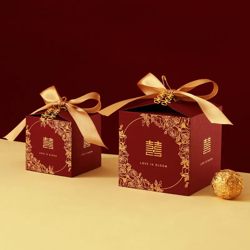 Red & Gold Double Happiness Chinese Wedding Favor Boxes gift boxes with gold ribbons and floral designs on a yellow surface.