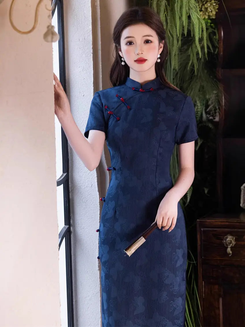 Woman in a Navy Blue Jacquard Butterfly Cheongsam – Mid-Length Modern Qipaostanding indoors with plants in the background