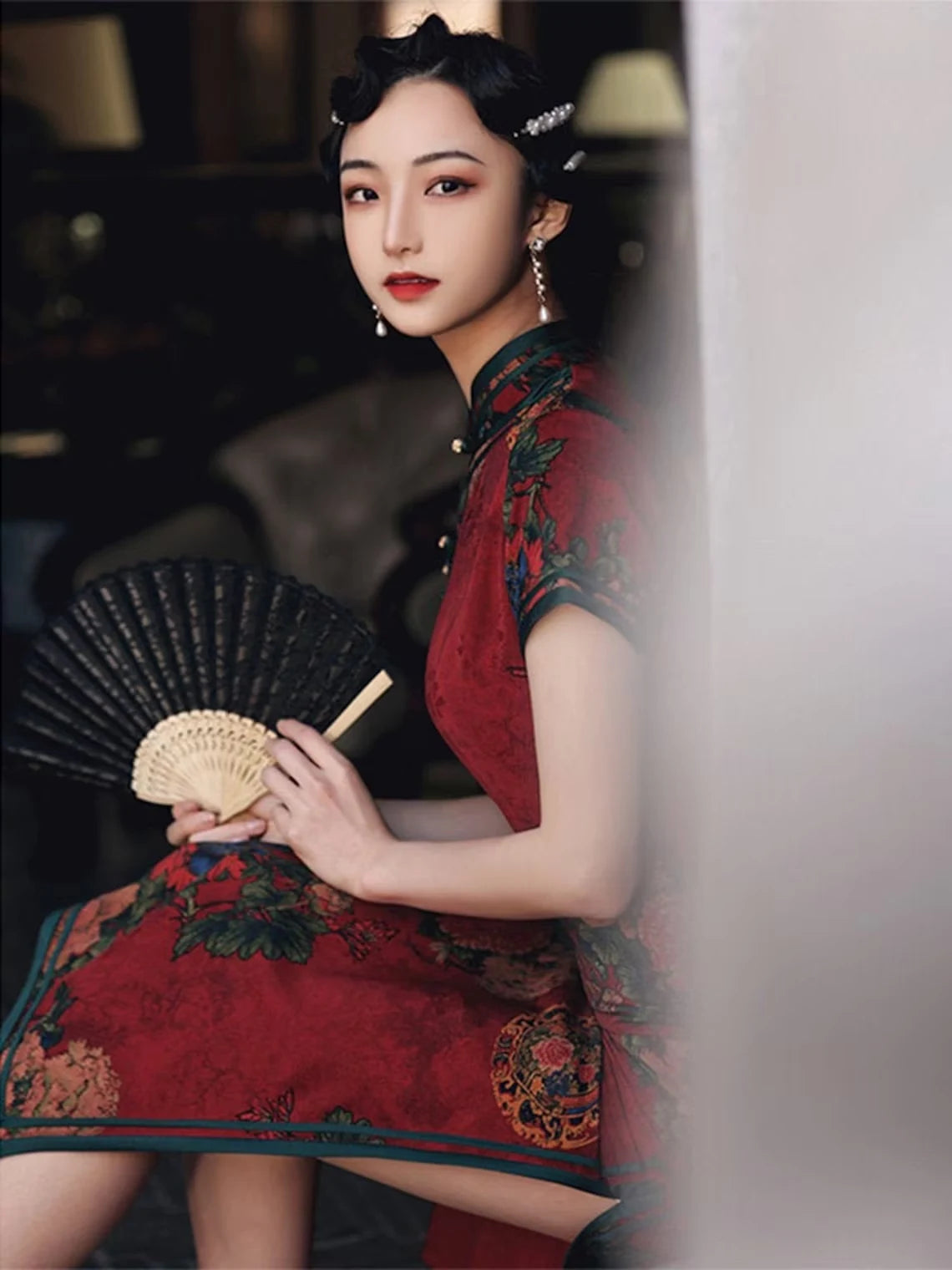 Woman in a traditional Vintage Red Chinese evening gown ,  Floral Qipao Cheongsam Dress holding a fan, with a blurred background.