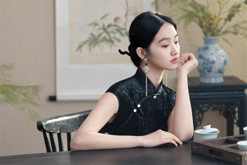Woman in a black traditional Chinese attire sitting at a table in a room with decorative elements