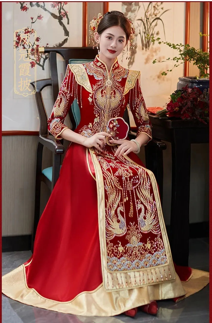 Woman in a traditional red and gold Chinese Velvet Wedding Qun Kwa Dress   with intricate patterns, sitting indoors.