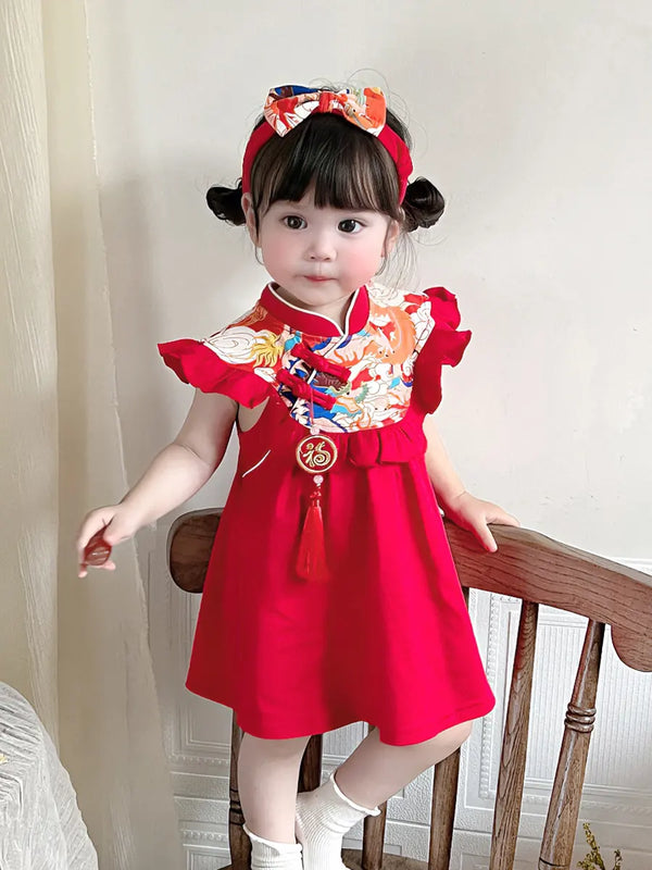 Child wearing a red traditional Baby Girl Chinese Tang Style  Qipao Dress with Headband  outfit with a colorful headband, standing on a wooden chair.