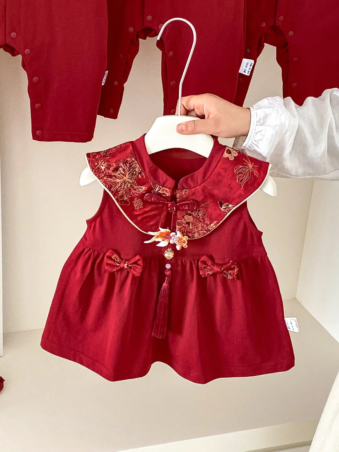 Baby Girl Red Traditional Chinese Summer Zhuazhou Ceremony Dress with floral embroidery and tassels on a hanger against a neutral background