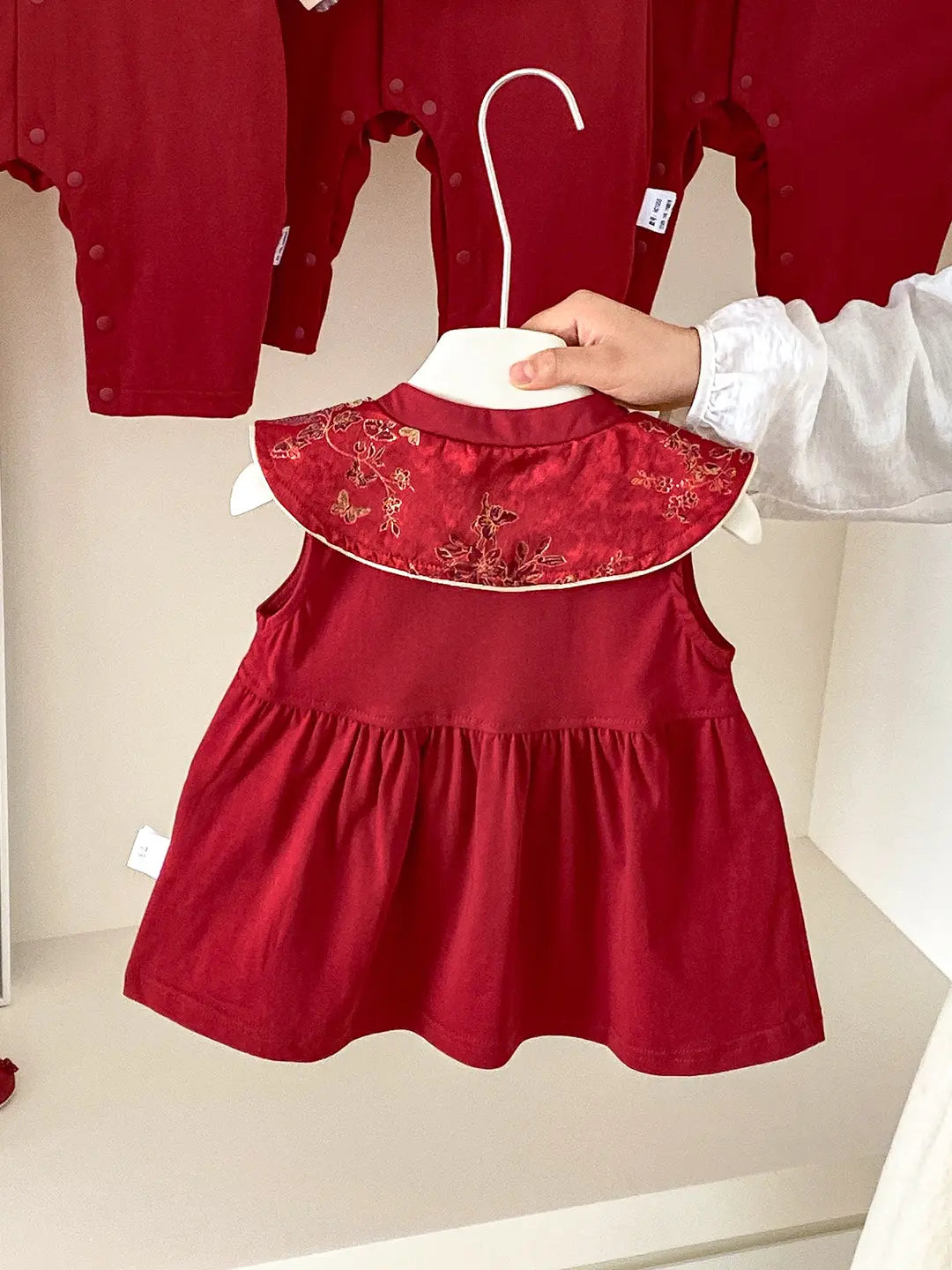 Baby Girl Red Traditional Chinese Summer Zhuazhou Ceremony Dress with floral embroidery on a hanger against a beige background