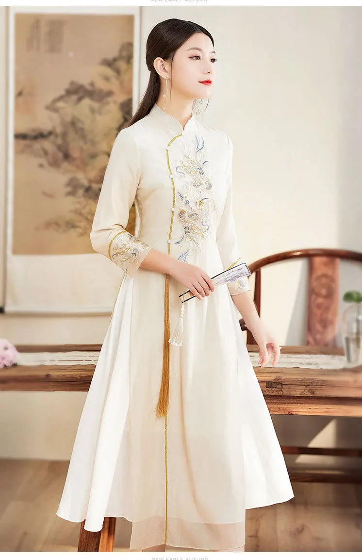 Woman in a traditional white Beige Ao Dai Style Qipao Dres – A-Line Long Cheongsam  in a room with wooden furniture and a painting.