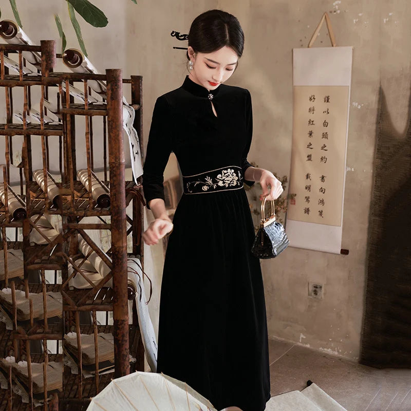 Woman in a Black 3/4 Long Sleeves A Line Velvet Qipao cheongsam Dress with   floral embroidery   standing in a room with wooden shelves and a wall scroll.