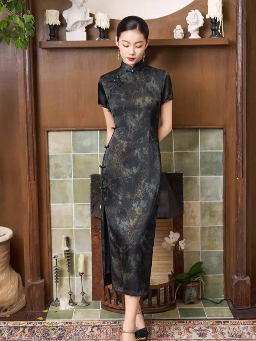 Woman in a Black & Deep Emeral Jacquard Satin Long Qipao With Green Buttons standing in a room with decorative elements.